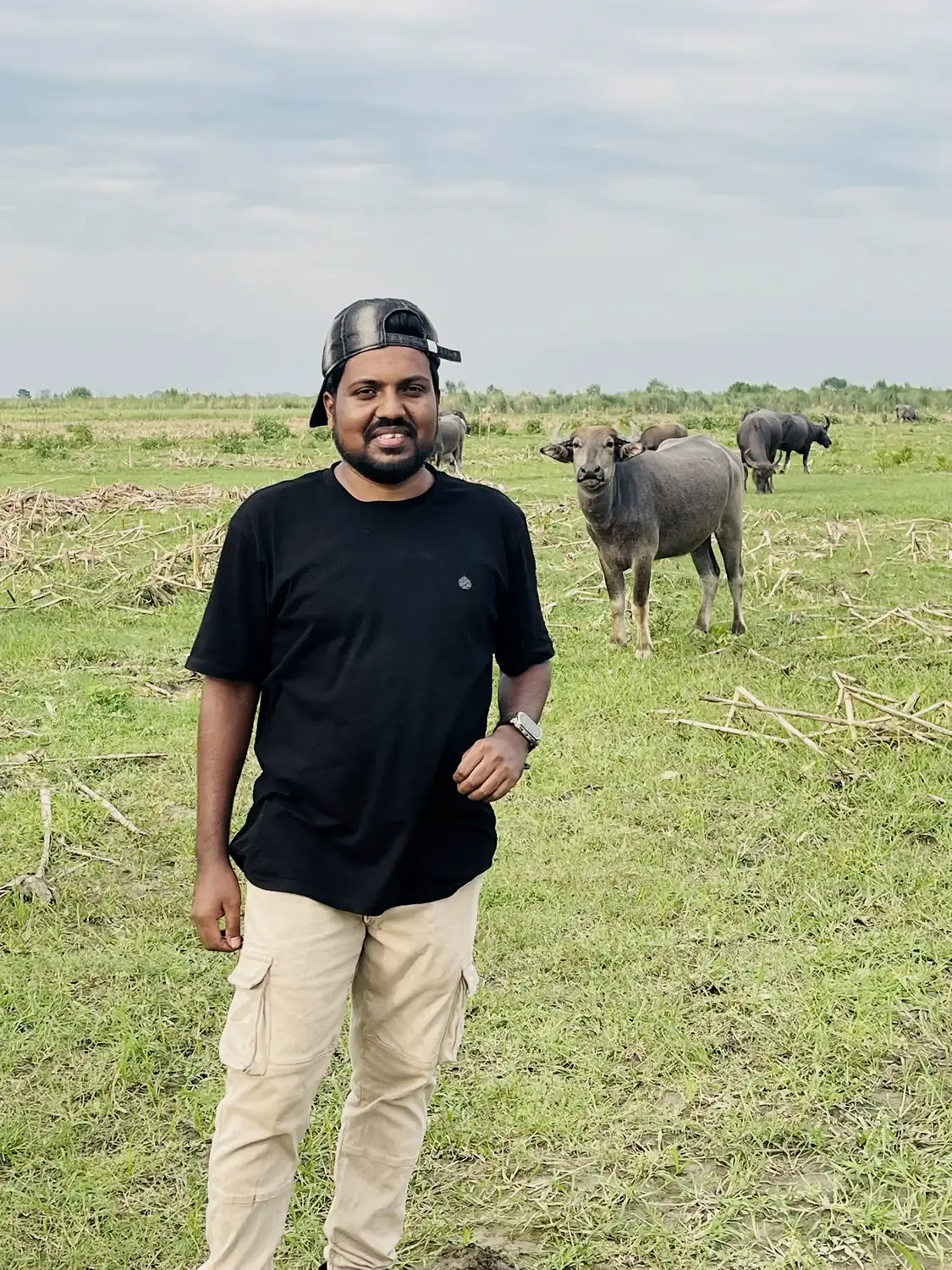Abdul Mannan Zinnat standing in a green field at the Abadi agri project, buffalo grazing behind him