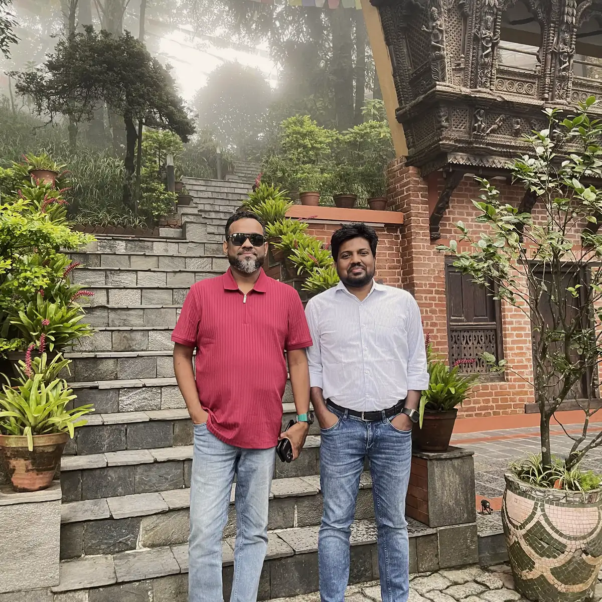 Abdul Mannan Zinnat and a friend on stone steps beside a carved wooden building